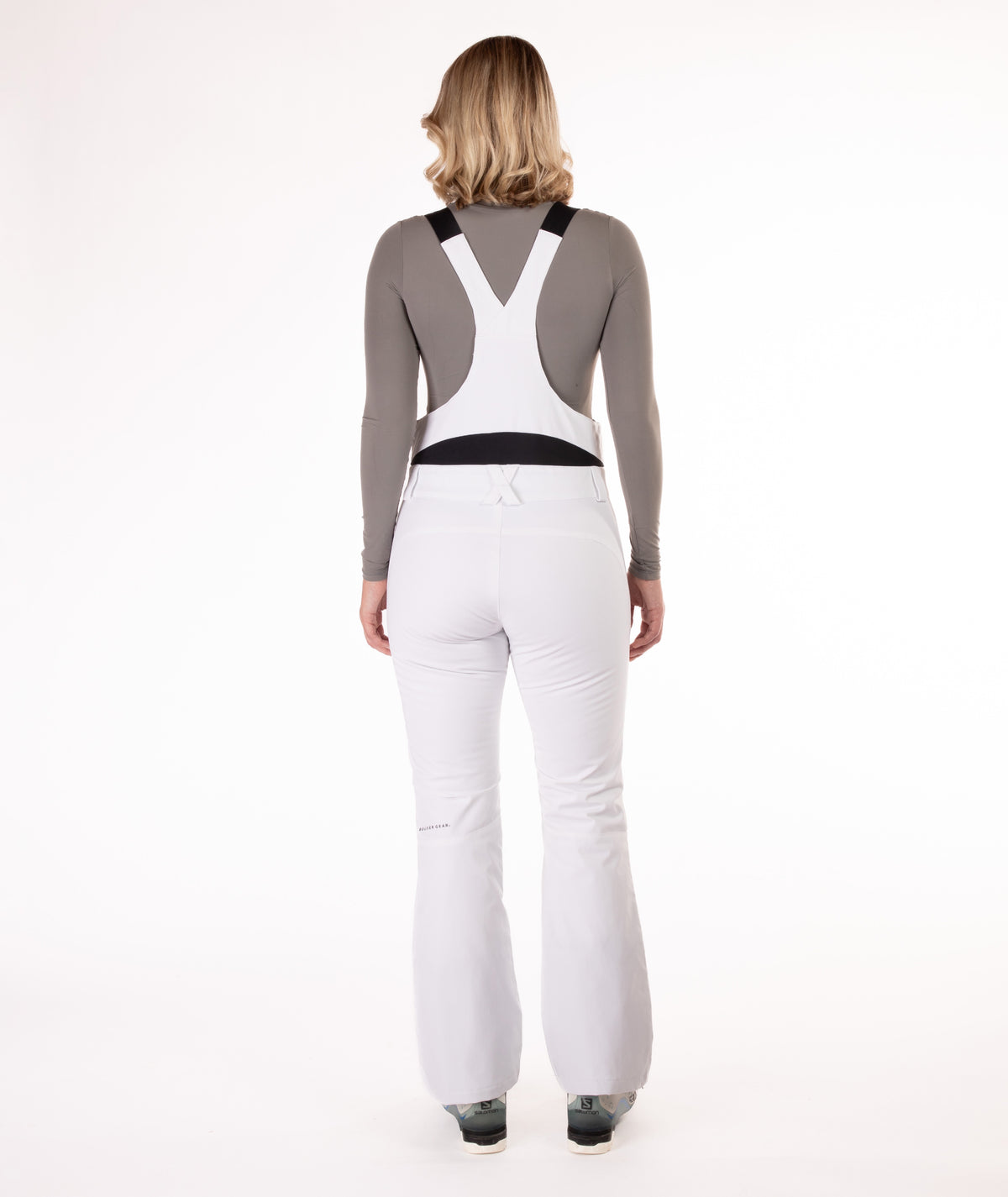 Back of person wearing a white snow bib overalls on a white background.