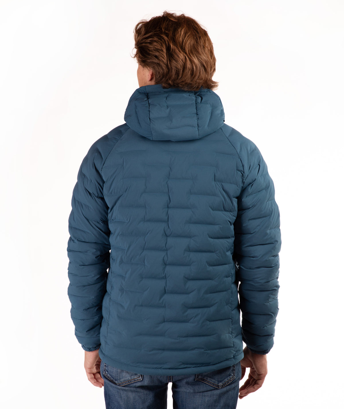 A person viewed from the back wearing a quilted hooded puffer jacket in a blue-teal color, paired with blue jeans, against a plain white studio background.