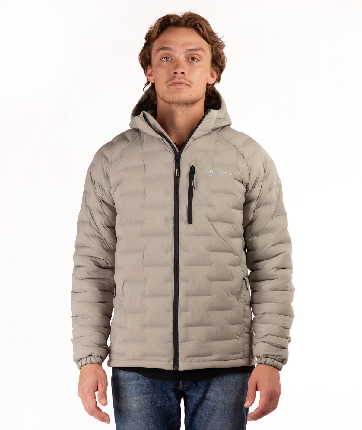 A man wearing a light beige hooded puffer jacket with black zippers, paired with blue jeans, photographed against a plain white background.