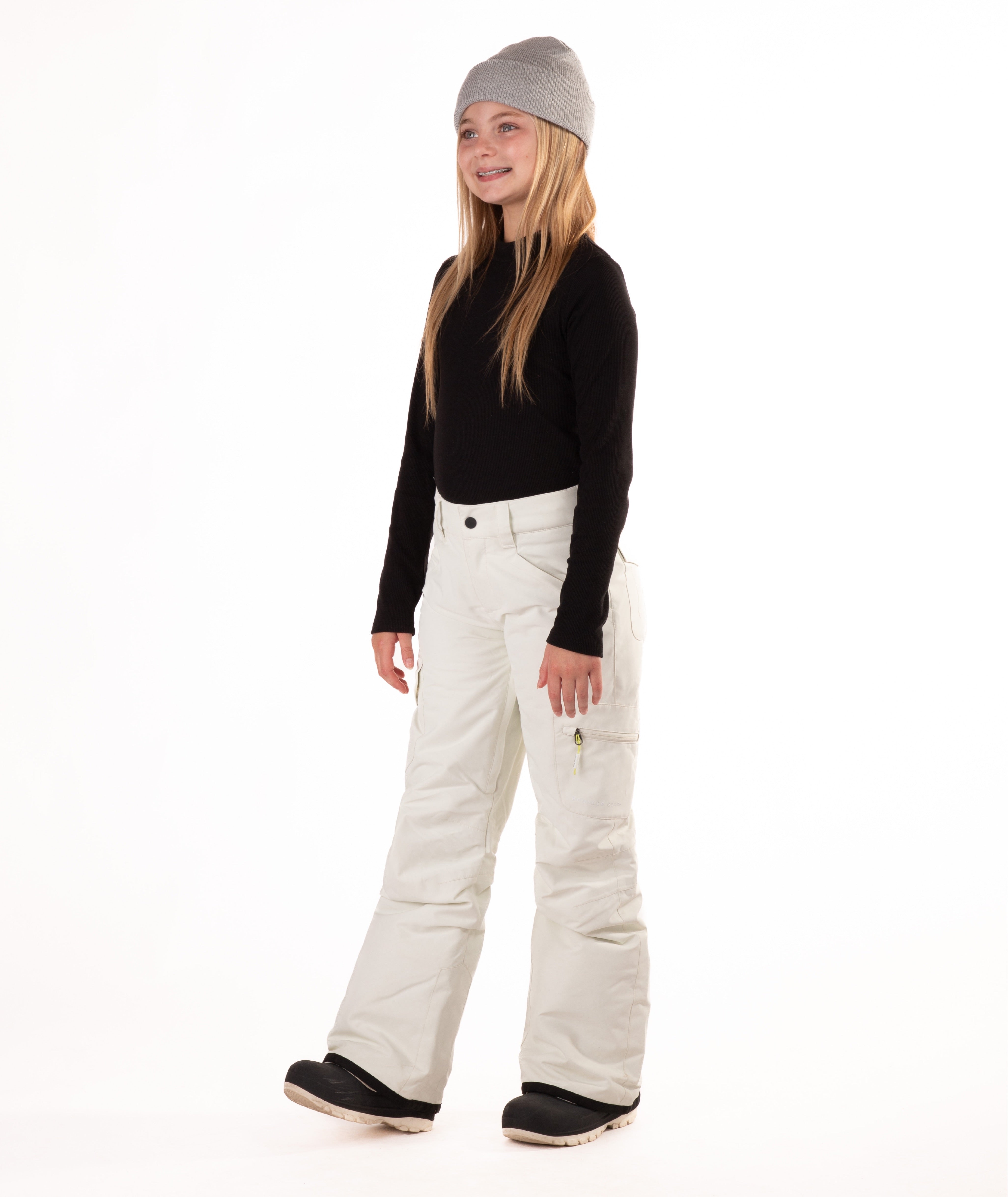 girl wearing cream colored snow pants and a black long-sleeve top on a white background