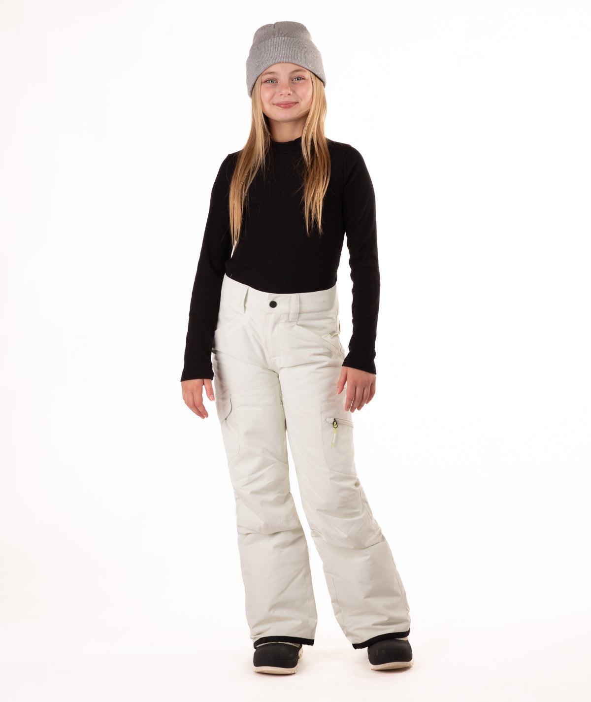 girl wearing cream colored snow pants and a black long-sleeve top on a white background