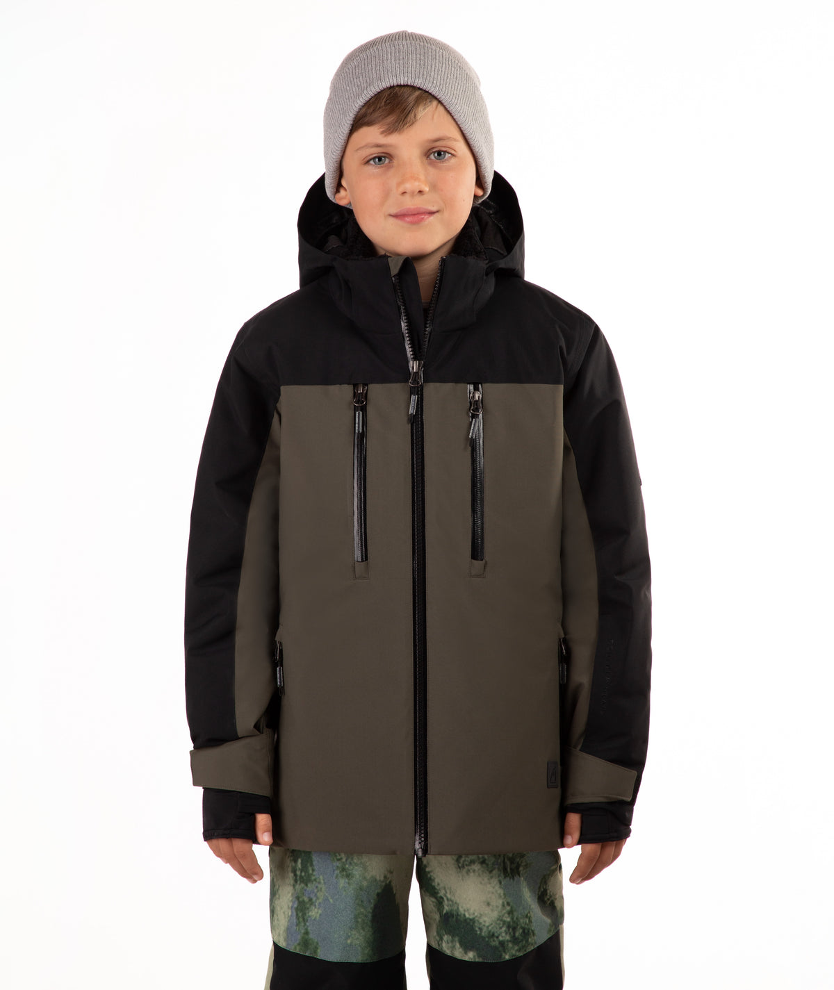 A child wearing a hooded ski jacket in black and olive green, paired with a light gray beanie and green camouflage-patterned pants, photographed against a plain white background.