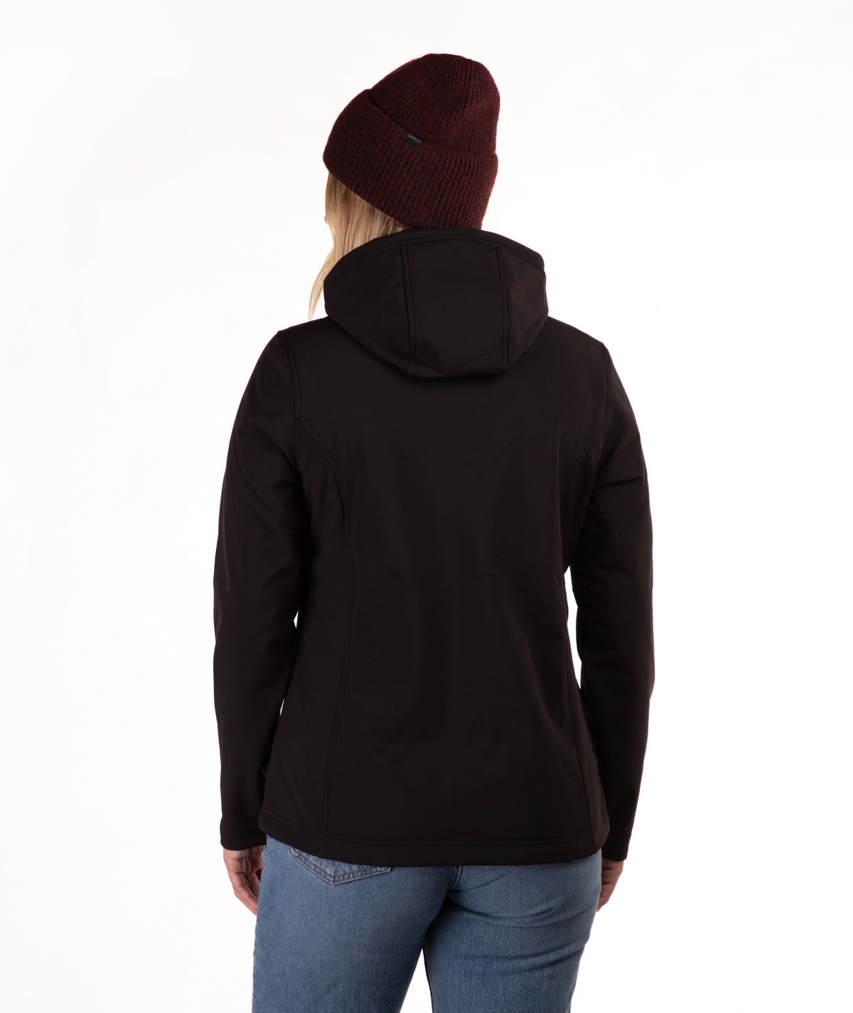 A woman viewed from the back wearing a black hooded jacket, a dark burgundy knit beanie, and blue jeans against a plain white studio background.