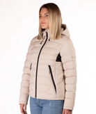 Woman wearing a beige puffer jacket with a black zipper on a white background