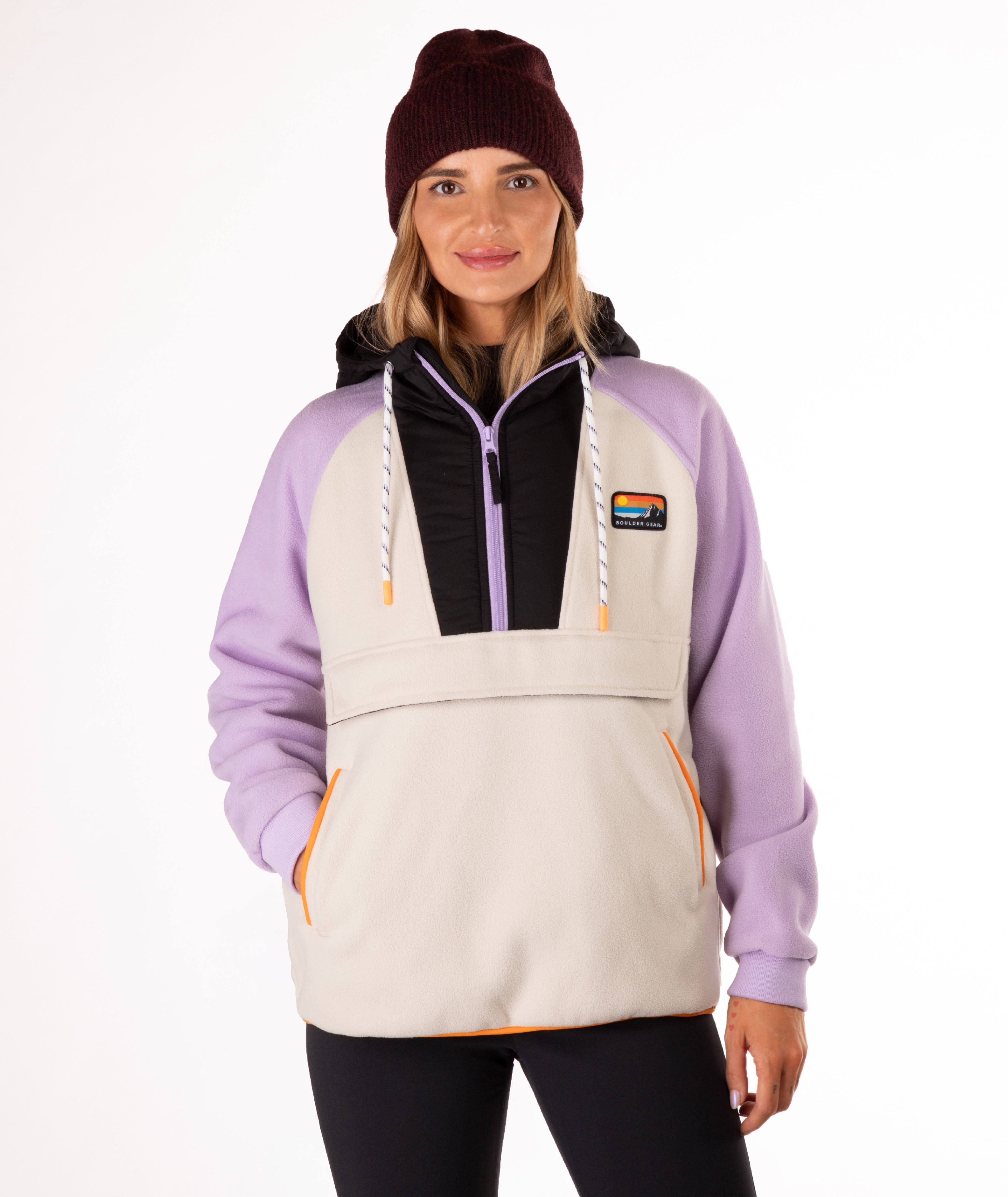 Woman wearing a light purple  and beige fleece pullover with a visible brand logo and orange detailing on a white background