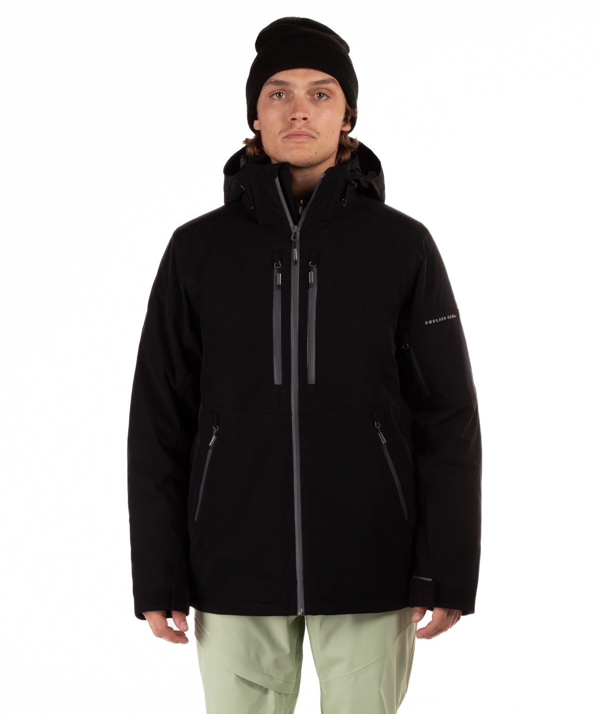 Person wearing a black jacket with gray zippers, light green pants and black beanie on a white background