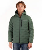 A man wearing a green hooded puffer jacket with a black front zipper and a small white logo on the left chest, paired with blue jeans, against a plain white background.