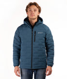 A man wearing a teal blue hooded puffer jacket paired with blue jeans, against a plain white background.