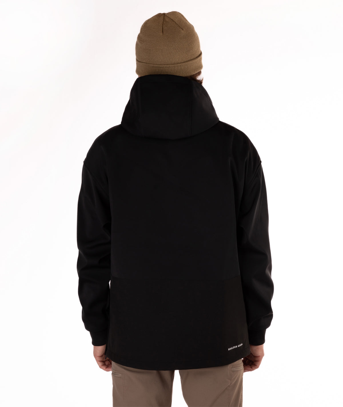 A person shown from the back wearing a black hooded jacket, a tan beanie, and tan pants against a plain white studio background.