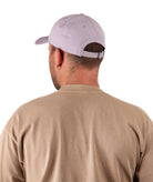 back of a Man wearing a light purple cap and beige shirt on a white background