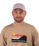 Man wearing a beige long-sleeve shirt with 'Boulder Gear' logo and a light purple cap on a white background