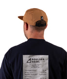 bak of a Person wearing a black Boulder Gear shirt and brown cap on a white background