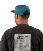 back of a Man wearing a black T-shirt and green cap with 'Boulder Gear' logo on a white background