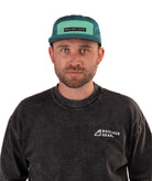 Man wearing a black T-shirt and green cap with 'Boulder Gear' logo on a white background