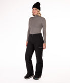 Person wearing a gray long-sleeve top and black snow pants on a white background