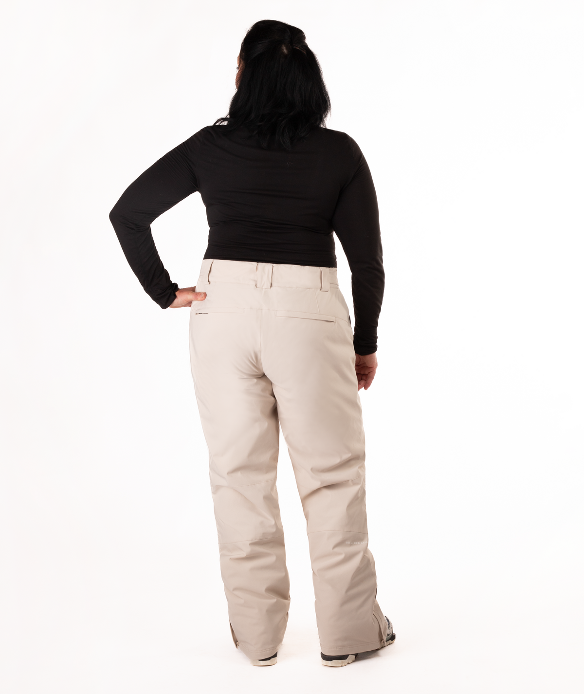 back of person wearing a black long-sleeve top and beige snow pants on a white background