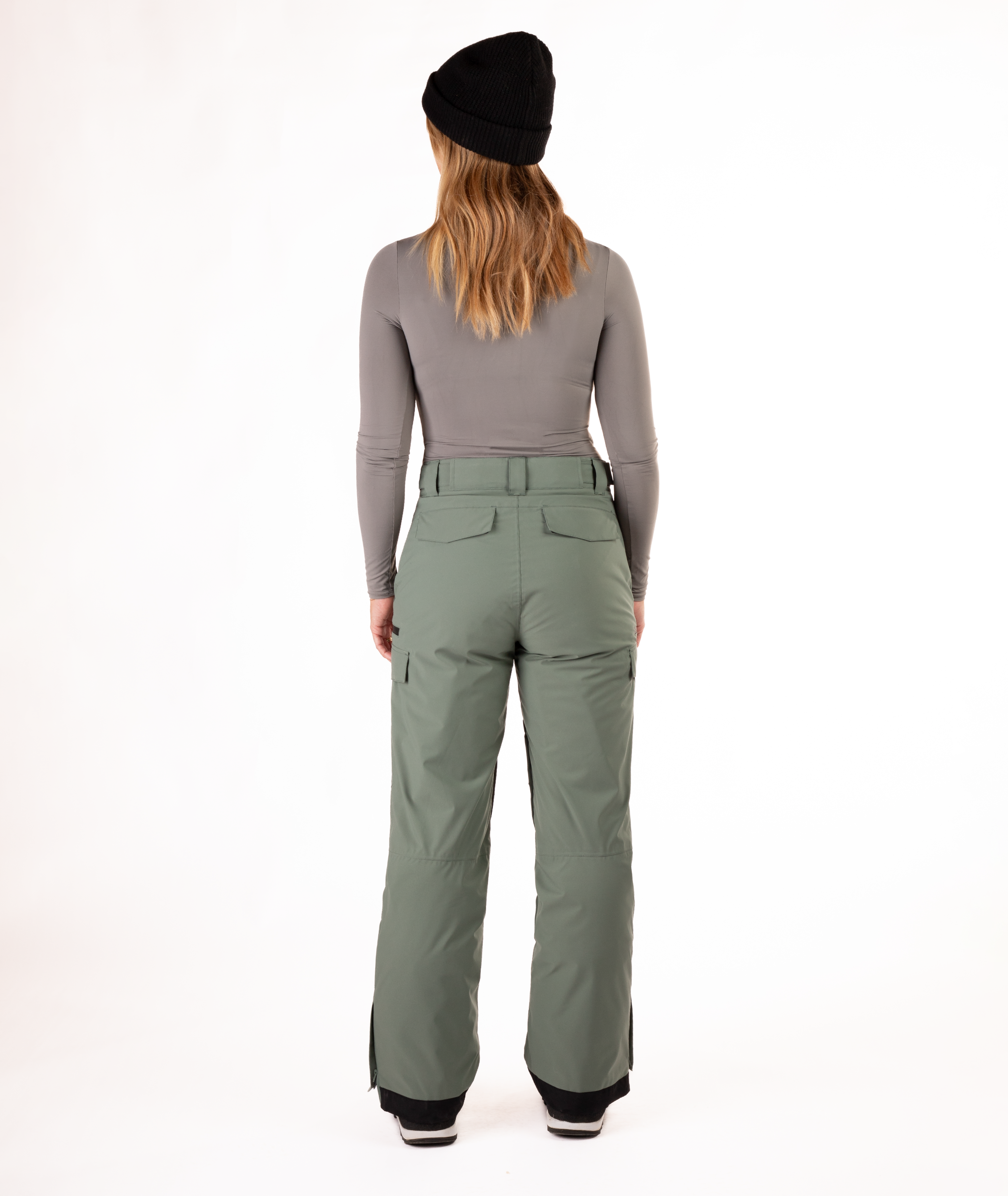 back of person wearing a gray long-sleeve top and green snow pants on a white background