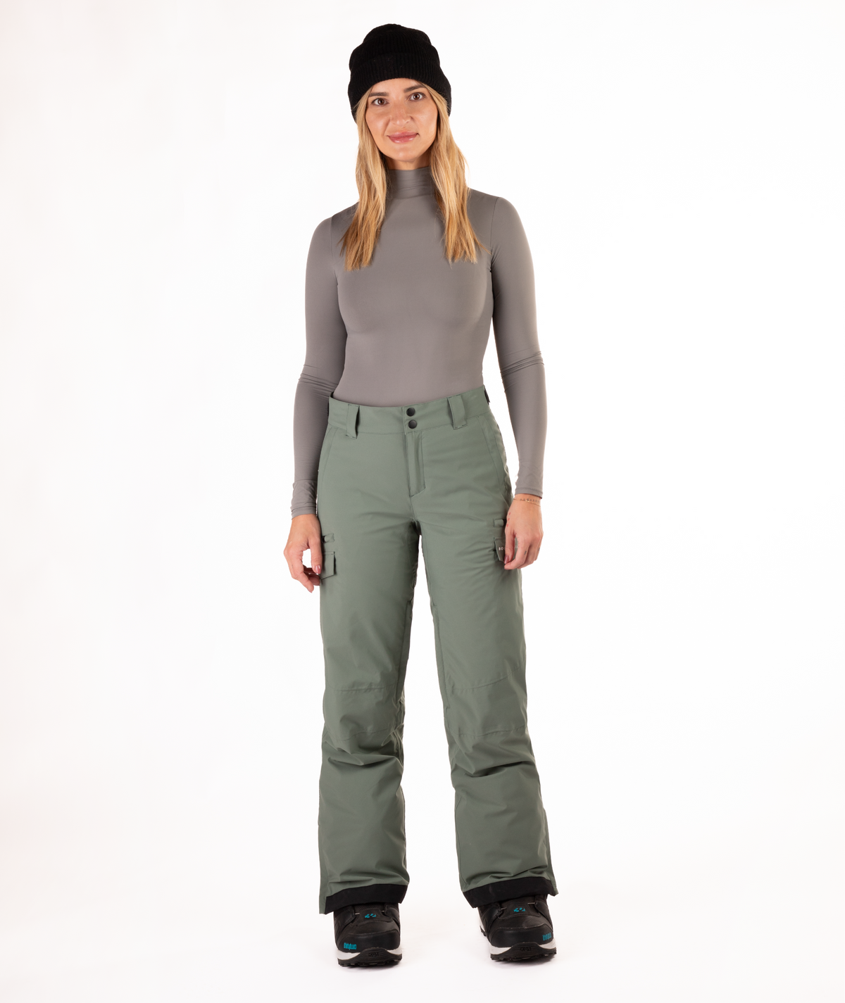 Person wearing a gray long-sleeve top and green snow pants on a white background