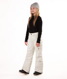 girl wearing cream colored snow pants and a black long-sleeve top on a white background