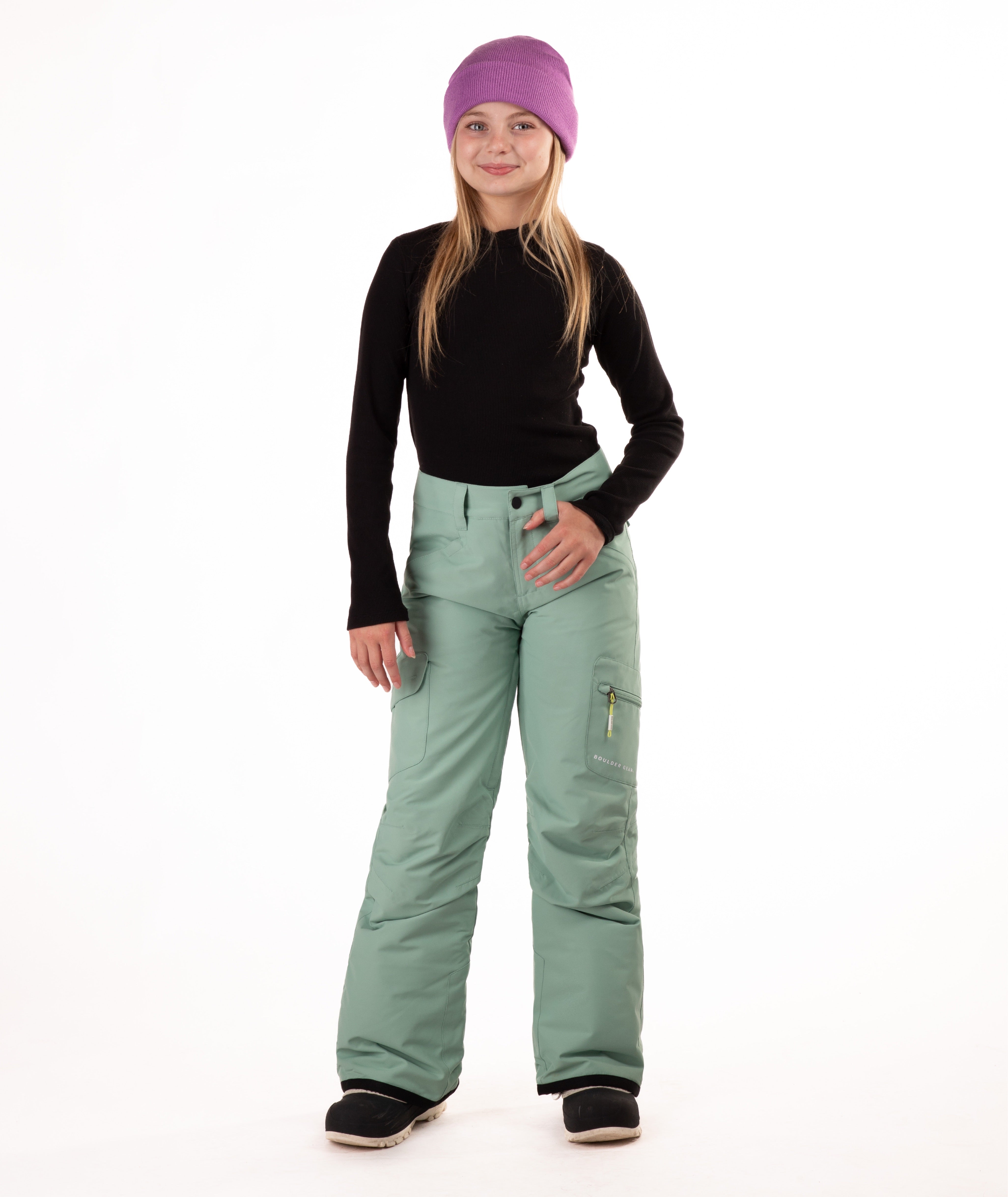 girl wearing green snow pants and a black long-sleeve top on a white background